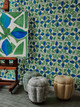 Fiori wallpaper, featuring a bold green and cobalt geometric floral pattern; paired with Unravel indoor woven fabric in Lemon on a bobbin stool.